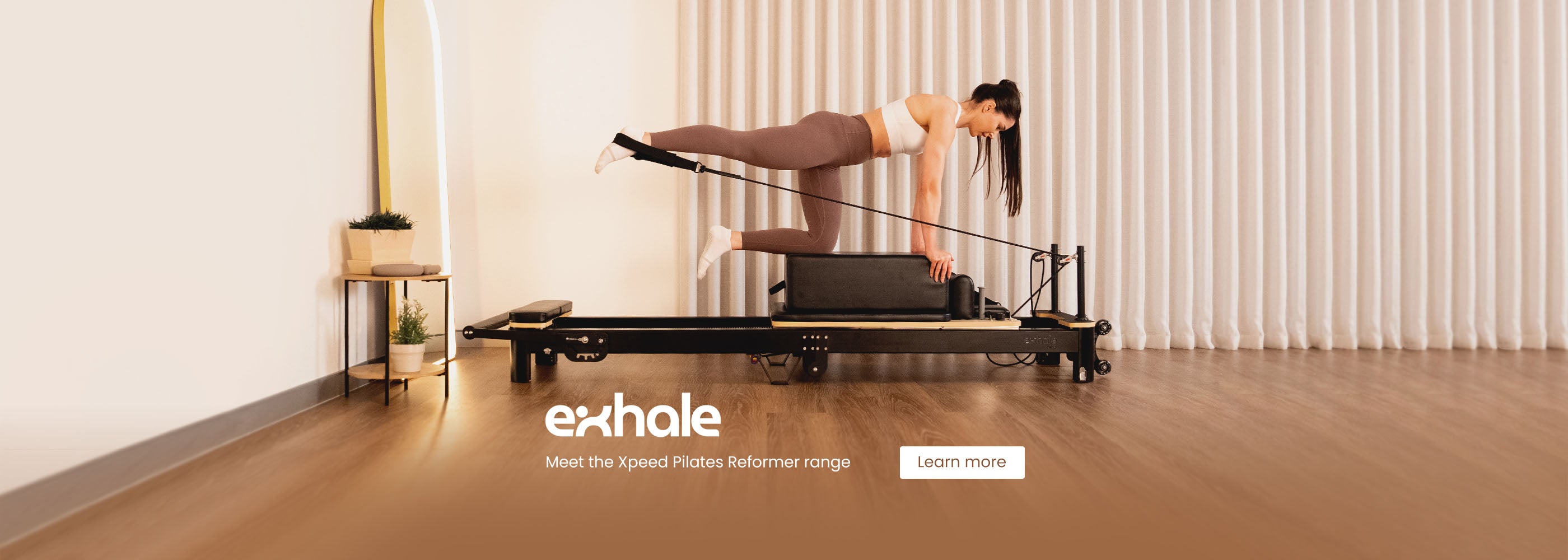 Woman using a reformer machine with 'exhale' branding in a minimalistic room.