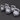 Five kettlebells in a staggered row on a dark gray surface, featuring matte gray bodies and light gray handles with small white circular stickers on the front.