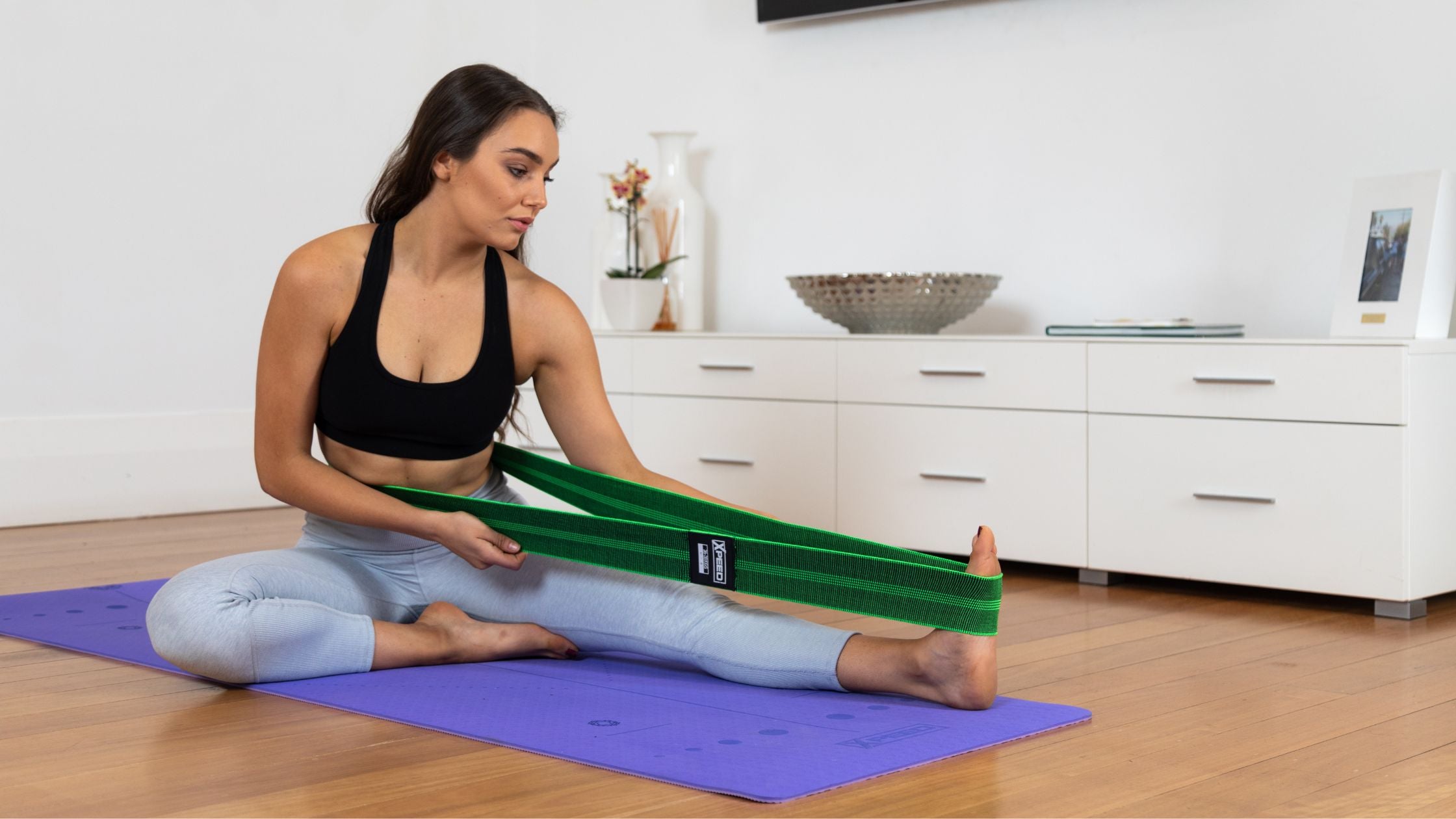 Malissa Fedele stretching hamstrings on a yoga mat with the Xpeed fabric stretch band